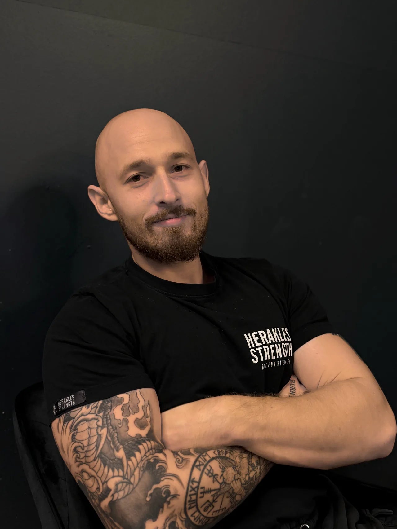 Leon Hiebler sitzt entspannt mit verschränkten Armen, Herakles-Strength-Shirt